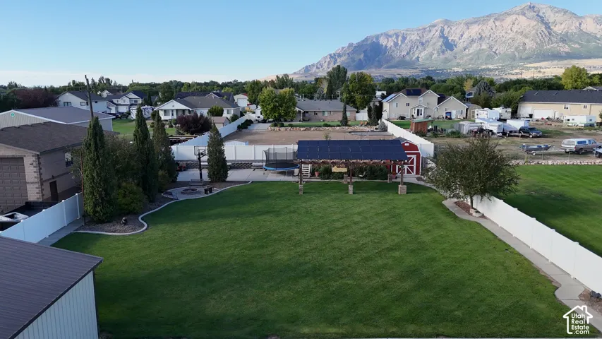 Expansive green lawn, white perimeter fencing, paved patio with fire pit, shaded pergola, and detached red shed