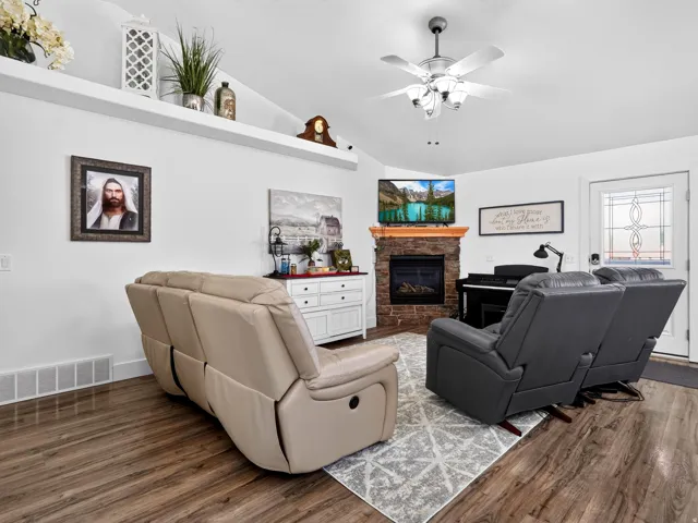Wood-finish flooring, a ceiling fan with integrated lighting, and a stone-surround fireplace with an electric insert