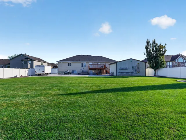 Expansive lawn with a white privacy fence, detached outbuilding, and mature tree