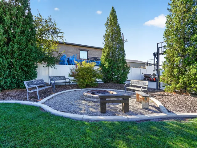 Manicured lawn with a gravel fire pit area, concrete curbing, mature evergreen trees, and a privacy fence