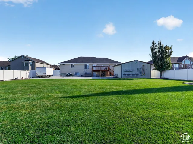 Expansive lawn with a white privacy fence, detached outbuilding, and mature tree