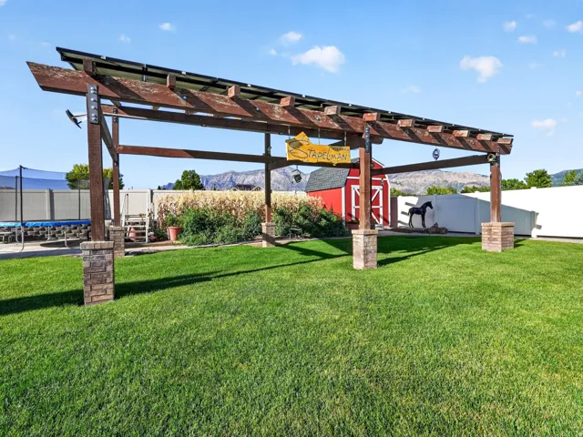 Wood pergola with stone-clad bases, expansive lawn area, red-painted barn structure, and mountain backdrop