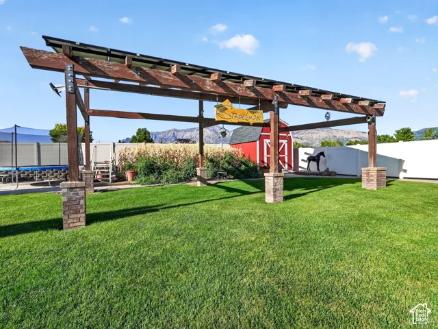 Wood pergola with stone-clad bases, expansive lawn area, red-painted barn structure, and mountain backdrop