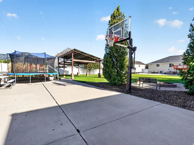 Concrete patio, mature landscaping, pergola, basketball hoop, and a stone-edged fire pit