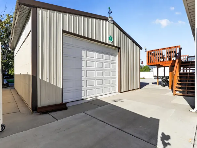 Corrugated metal exterior with a single garage door, concrete drive, and an exterior wood deck with stairs