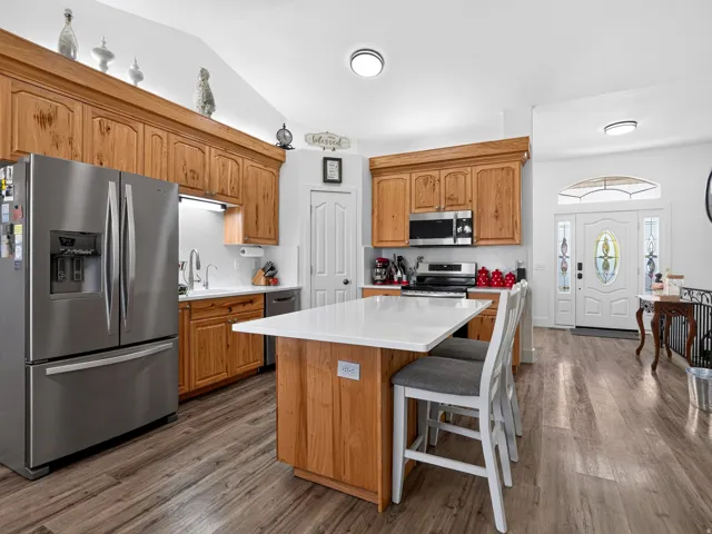 Wood-finish flooring throughout, kitchen island with seating, stainless steel appliances, wood cabinetry, and a decorative front door with stained glass accents