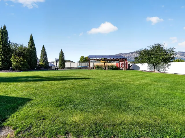 Expansive green lawn with mature evergreen trees, a white perimeter fence, a red barn structure, and a pergola with solar panels
