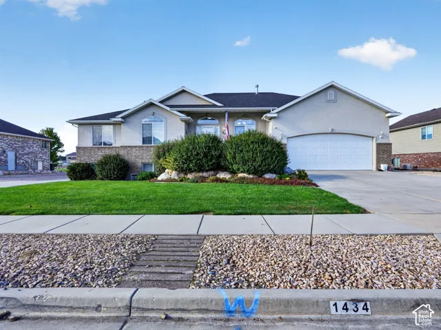 Stucco exterior with brick accent, attached garage, manicured lawn, and established shrubbery