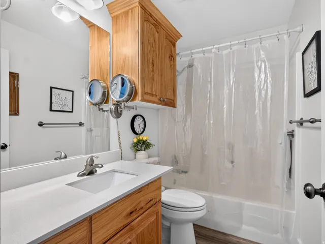 Bathroom featuring a single vanity with a white countertop and integrated sink, wood-finish cabinetry, built-in overhead cabinet, and a shower-over-tub combination