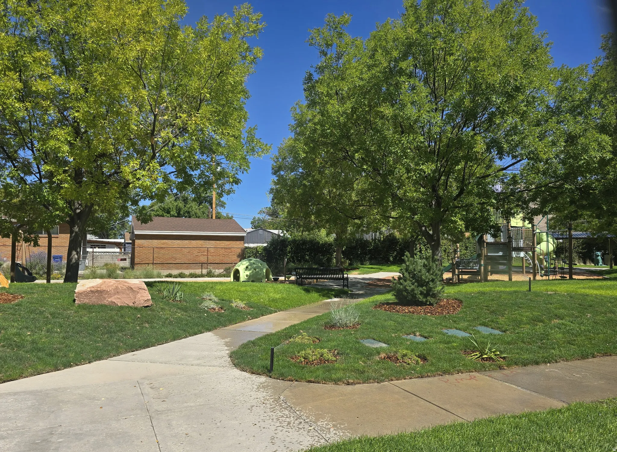 Manicured green space featuring mature trees, a concrete pathway, and landscaping