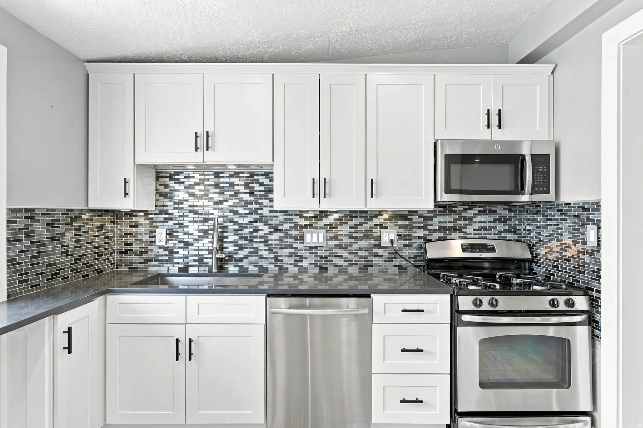 White shaker cabinetry, mosaic tile backsplash, stainless steel appliances, solid surface countertops, and an undermount sink