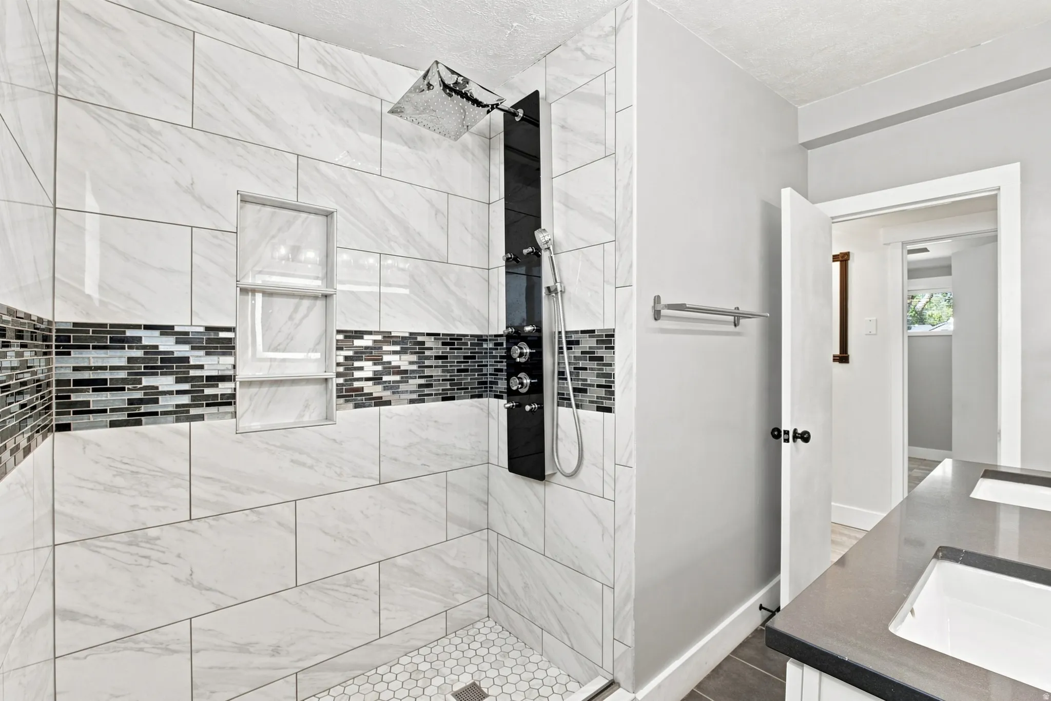 Walk-in shower with large format wall tiles, mosaic accent band, integrated shower niche, and hex tile floor