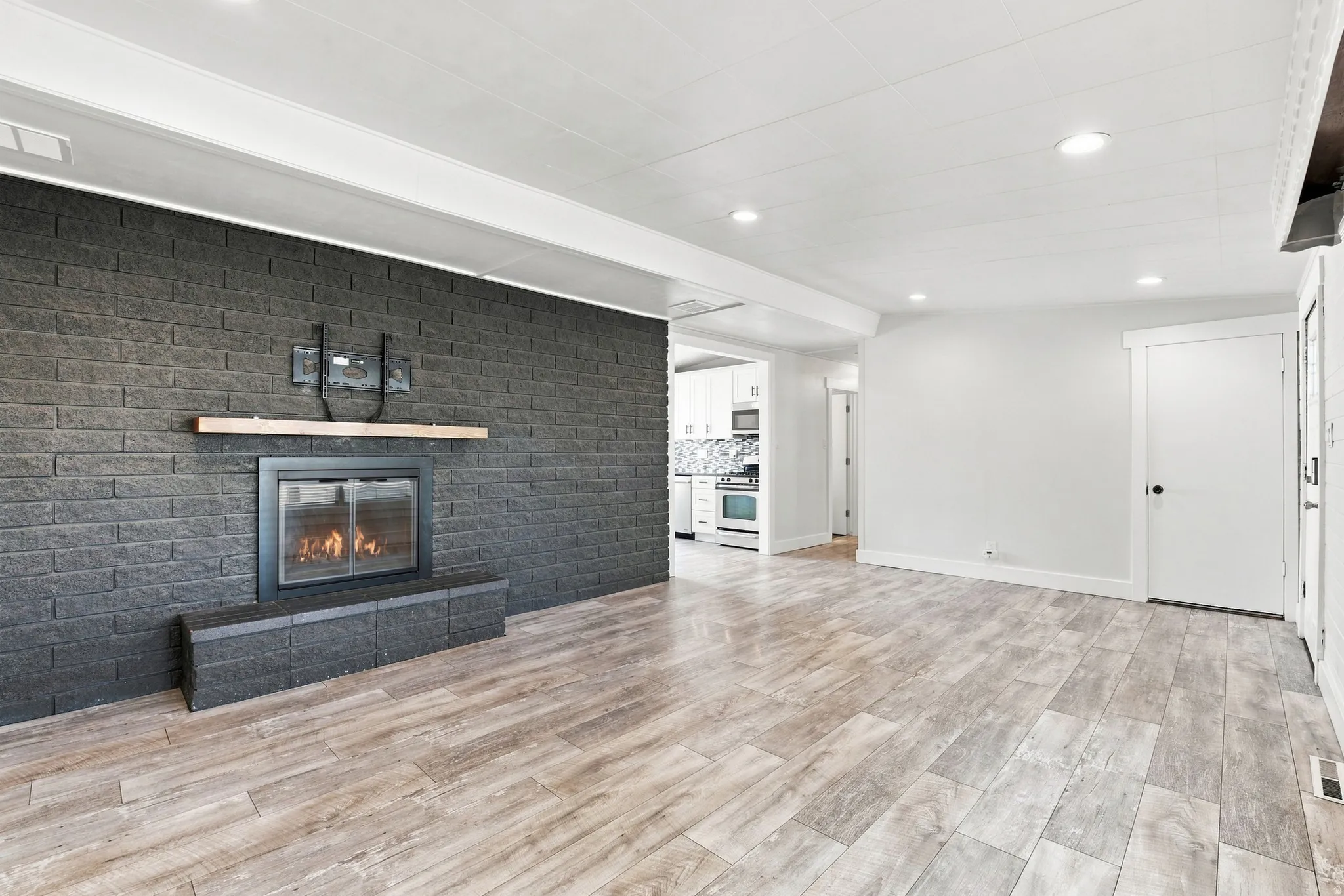 Wood-finish flooring, recessed lighting, and a dark brick fireplace with a wood mantel