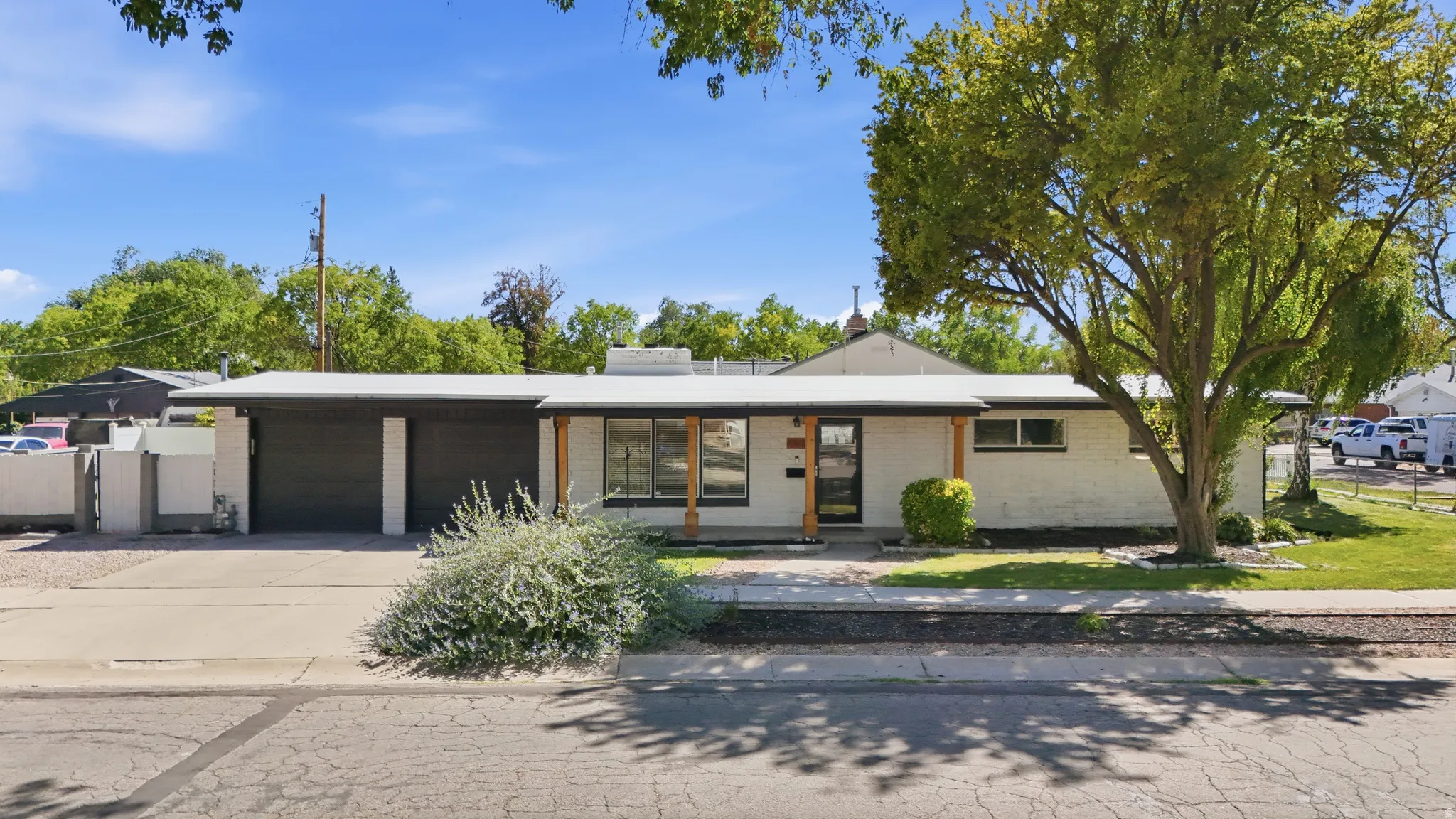 Mid-century modern exterior featuring white brick, dark garage doors, and natural wood support beams