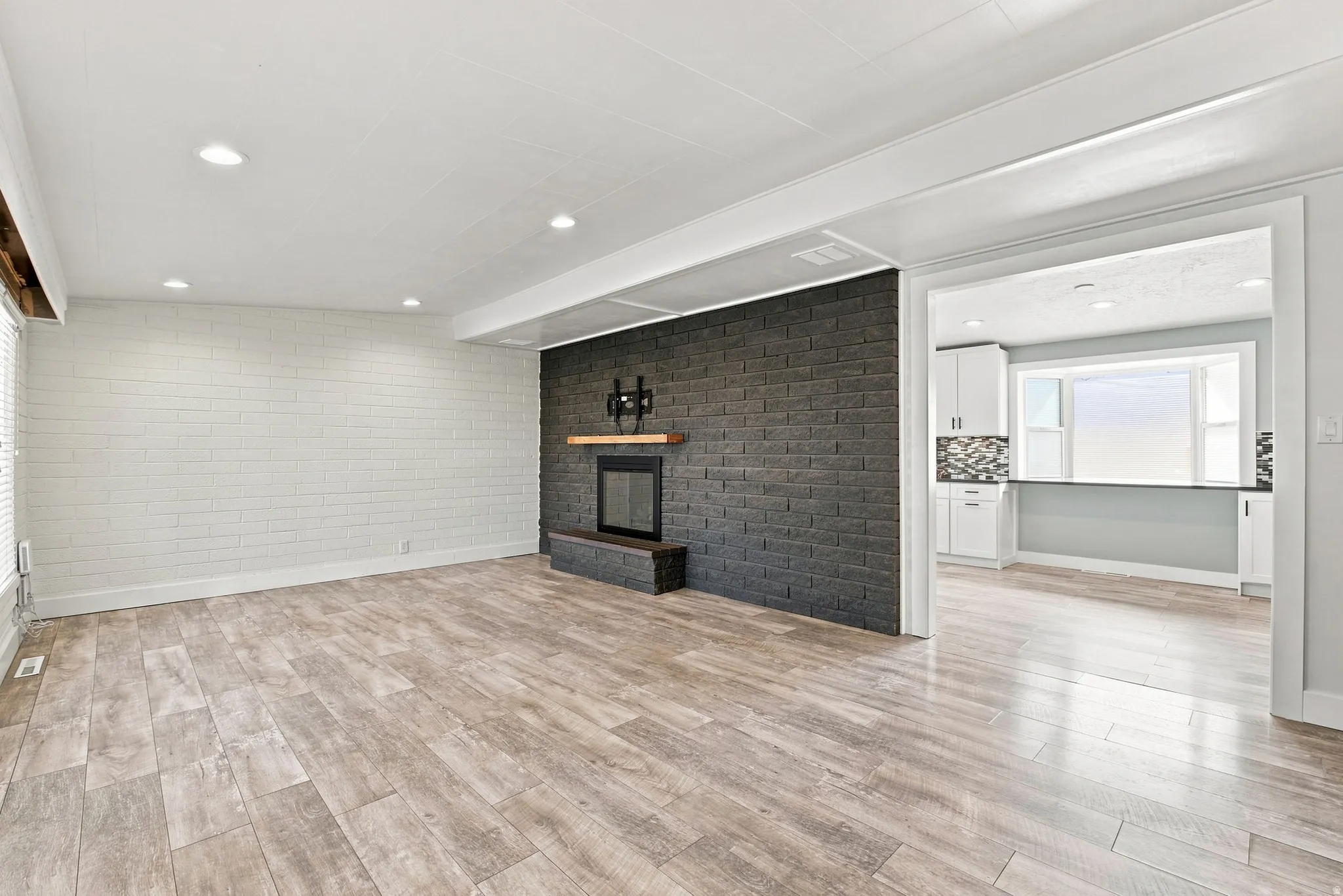 Expansive room featuring wood-finish flooring, a contemporary fireplace with a dark brick surround, and recessed lighting