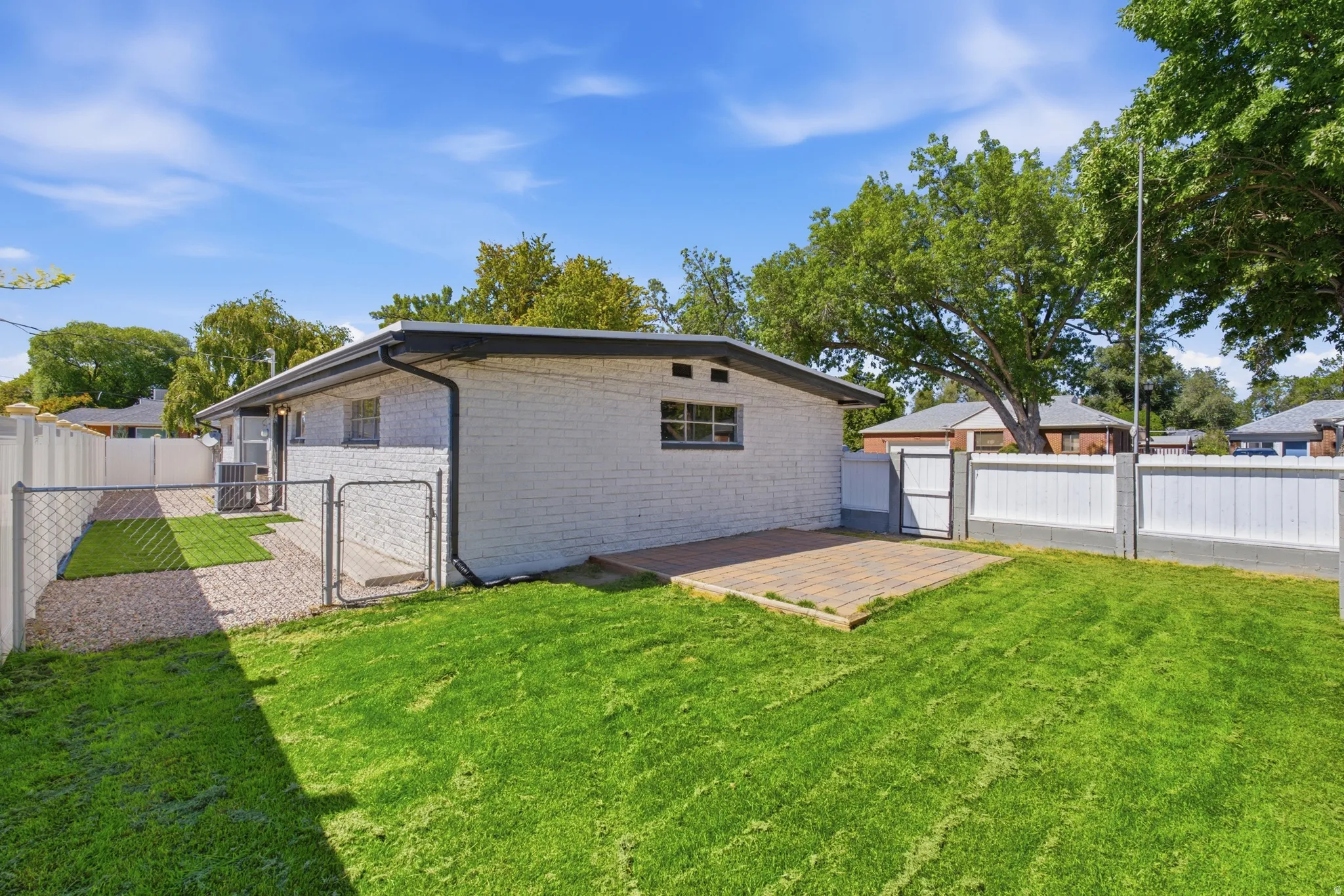 Expansive lawn area, paver patio, chain-link fencing, privacy fencing, and a white brick exterior
