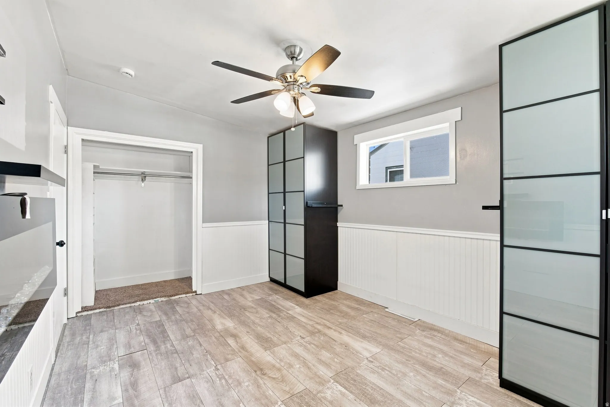 Wood-finish flooring, white beadboard wainscoting, and a ceiling fan with integrated lighting