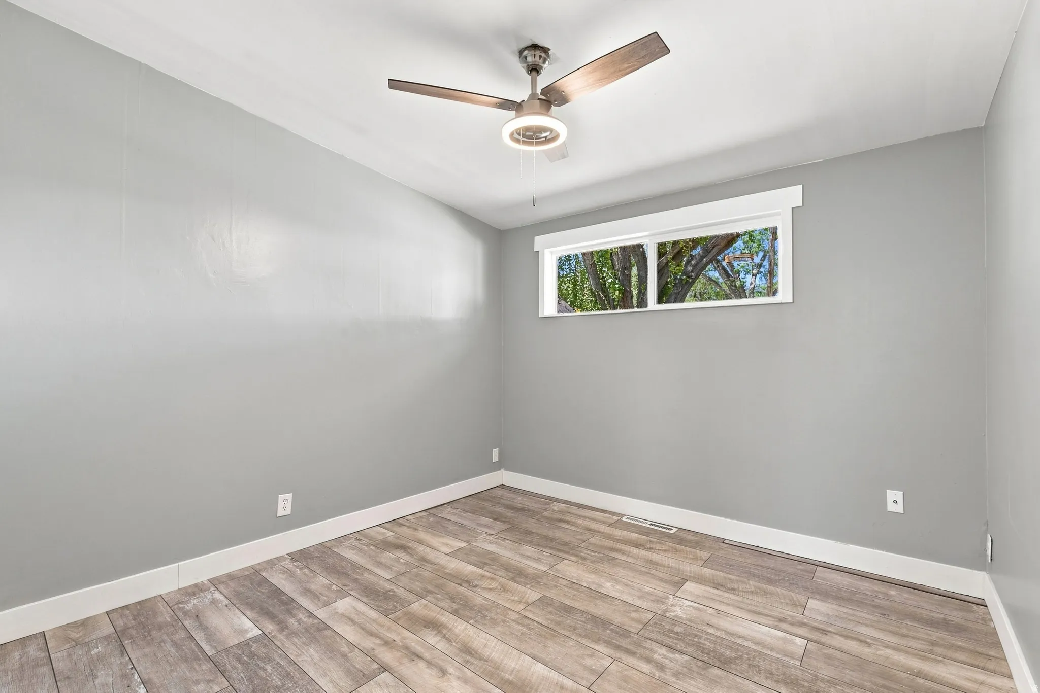 Wood-finish flooring, neutral gray wall tones, ceiling fan, and a transom window