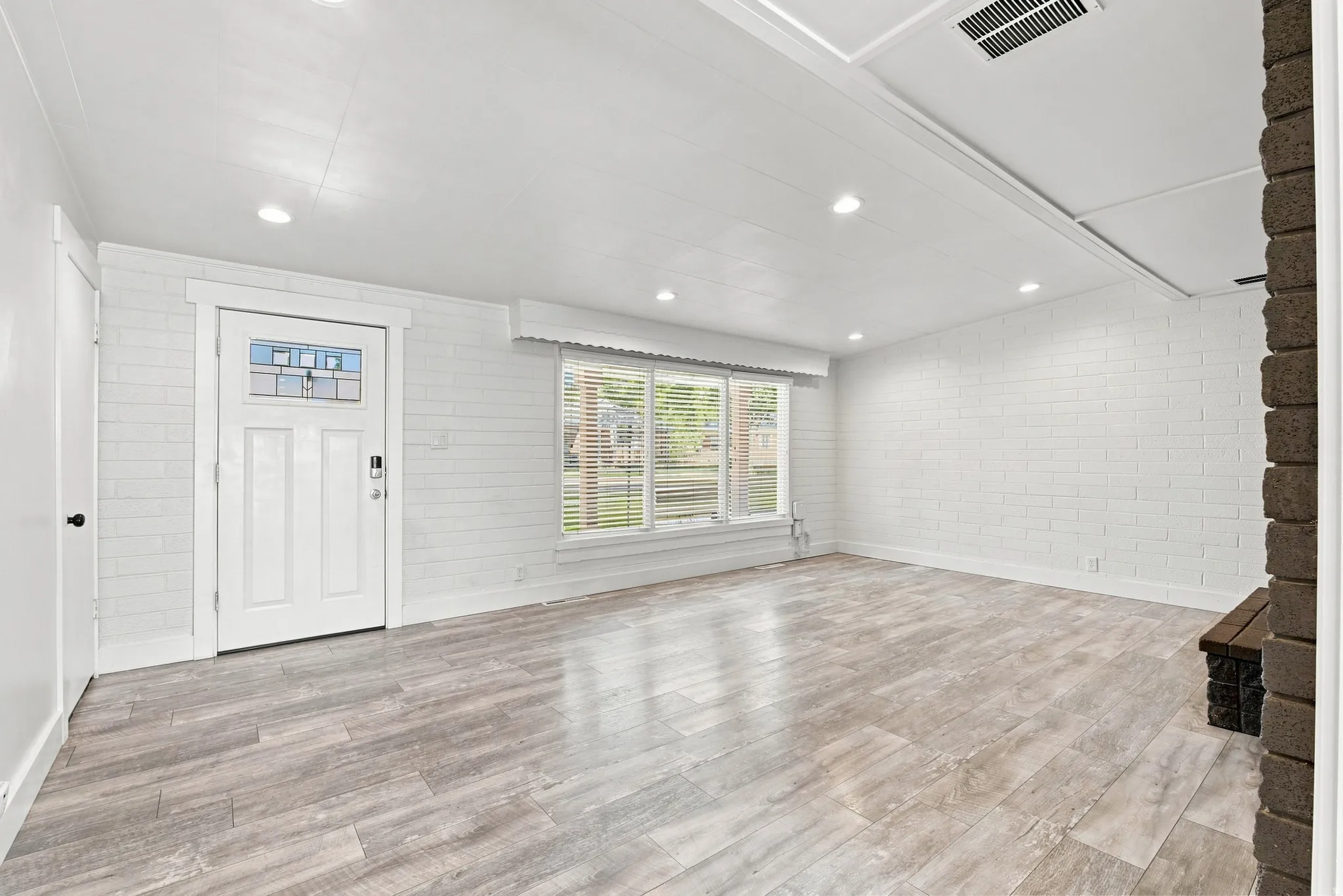 Bright living area featuring wood-finish flooring, recessed lighting, and white painted brick walls