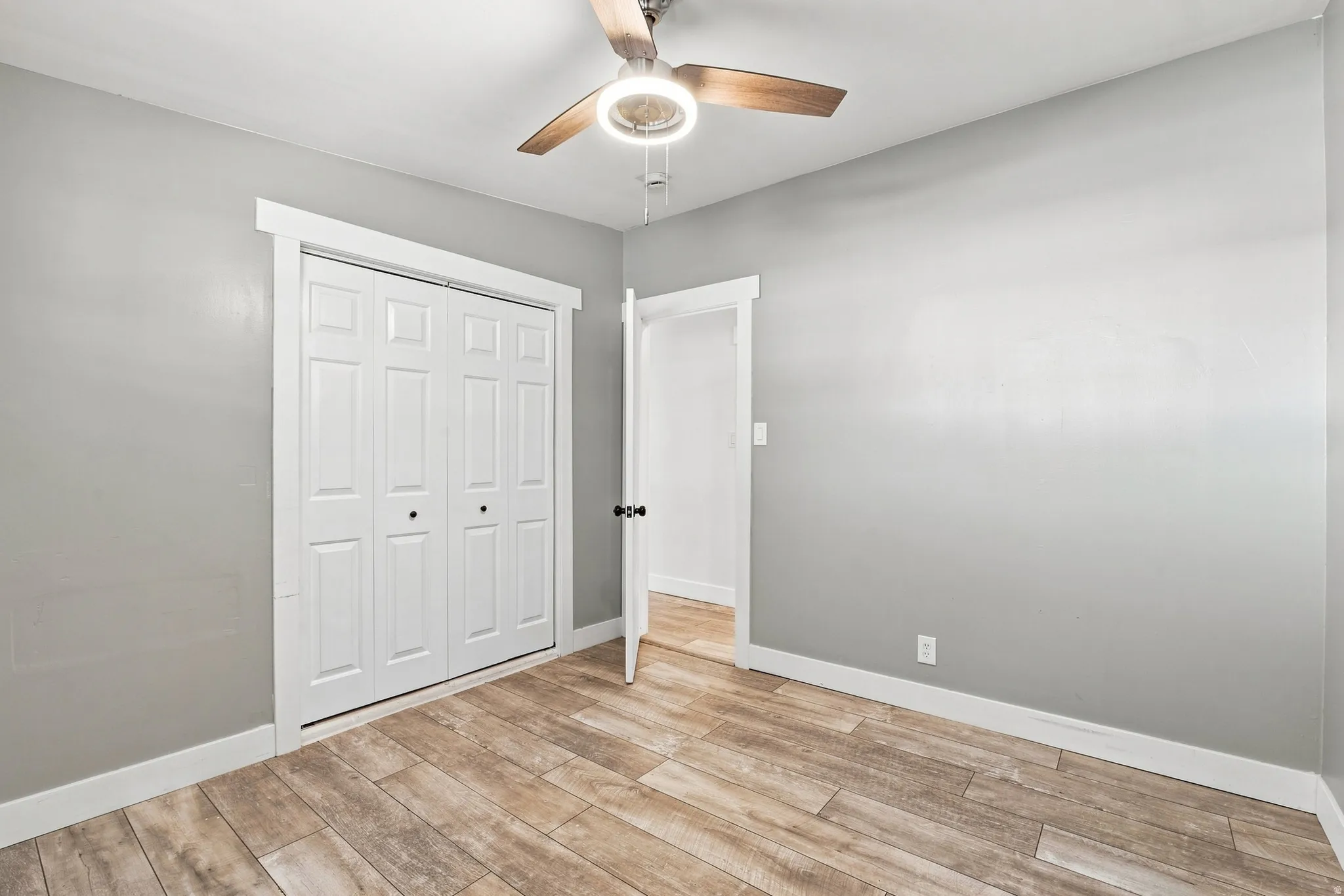 Wood-finish flooring, white trim, bi-fold closet doors, and a ceiling fan