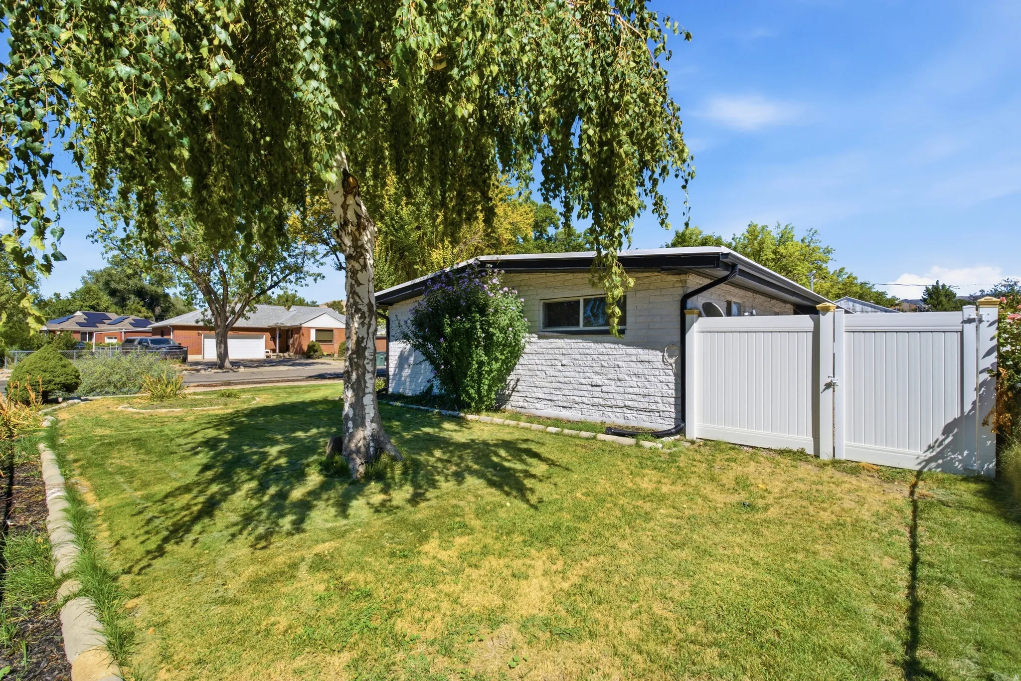 Lawn area with mature tree, white privacy gate, and stone-finish exterior