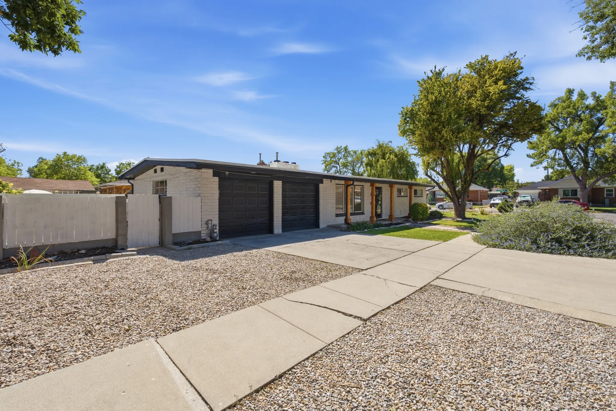 White brick exterior with a flat roofline, two-car garage with black doors, covered front entry with wood columns, and a concrete driveway