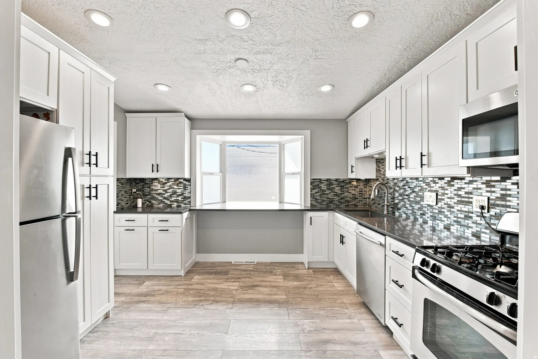 White shaker cabinetry, stainless steel appliances, dark countertops, a tiled backsplash, and recessed lighting
