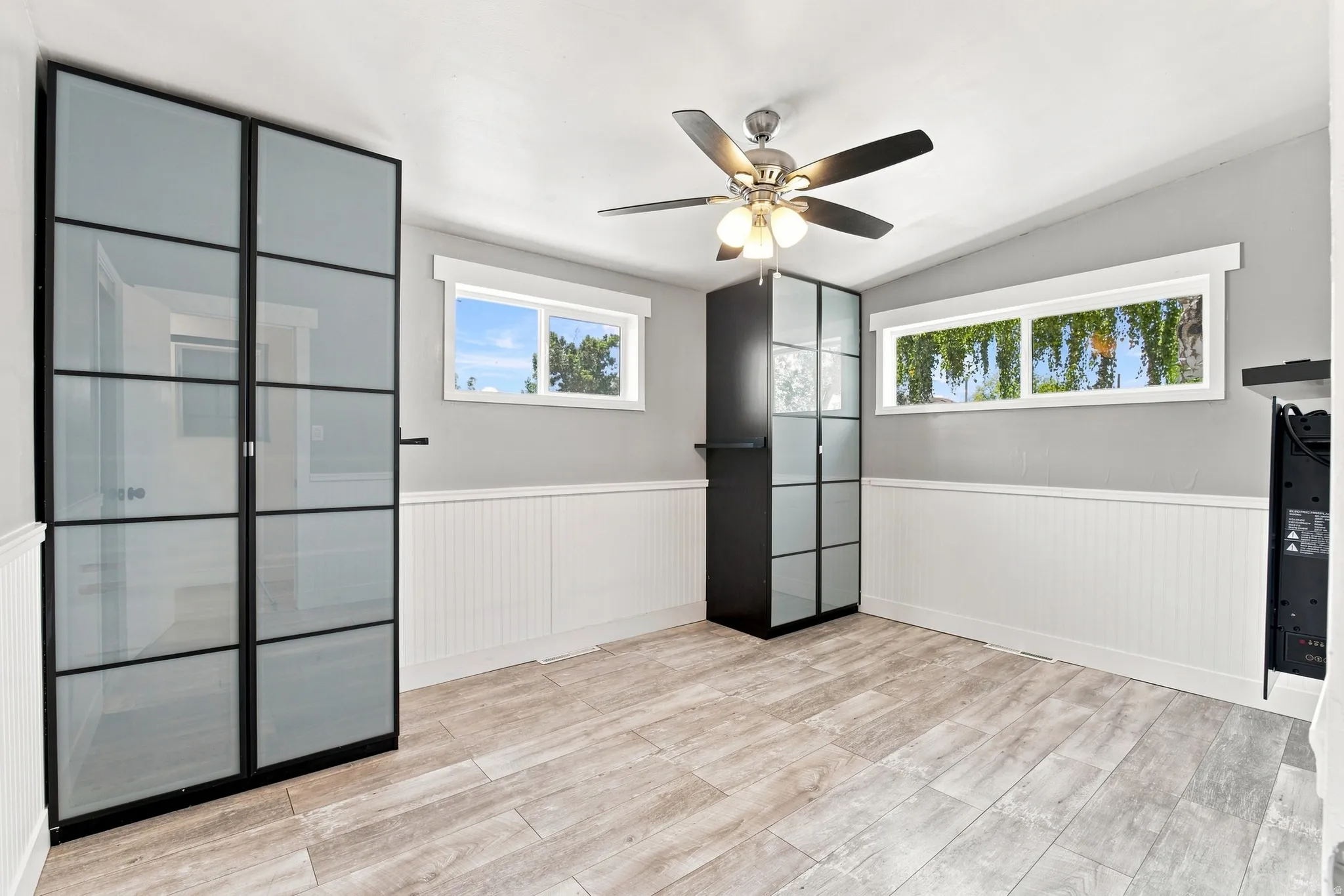 Light wood-finish flooring, white wainscoting, and a ceiling fan with integrated lighting
