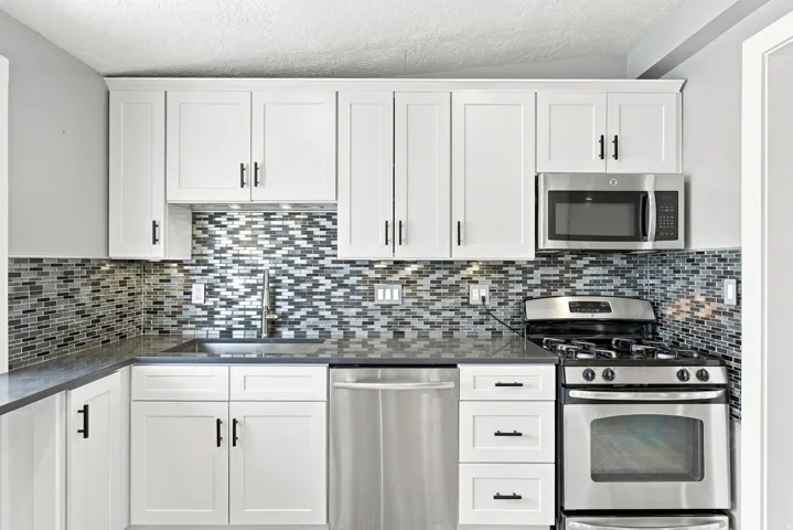 White shaker cabinetry, mosaic tile backsplash, stainless steel appliances, solid surface countertops, and an undermount sink