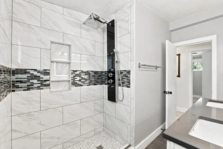 Walk-in shower with large format wall tiles, mosaic accent band, integrated shower niche, and hex tile floor
