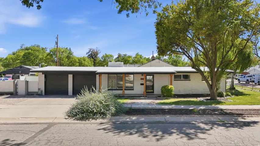 Mid-century modern exterior featuring white brick, dark garage doors, and natural wood support beams