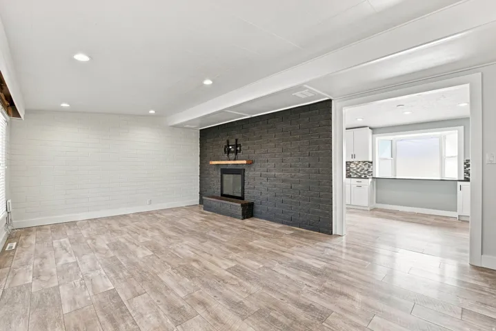 Expansive room featuring wood-finish flooring, a contemporary fireplace with a dark brick surround, and recessed lighting
