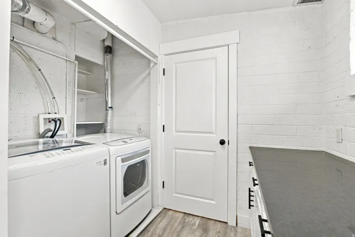 Laundry area featuring wood-finish flooring, white painted block walls, built-in shelving, and a dark countertop