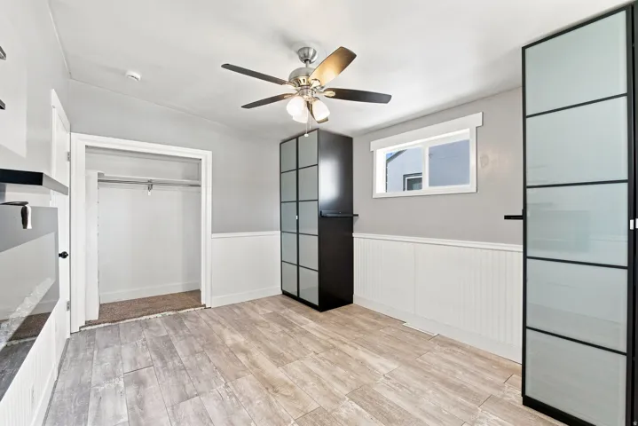 Wood-finish flooring, white beadboard wainscoting, and a ceiling fan with integrated lighting