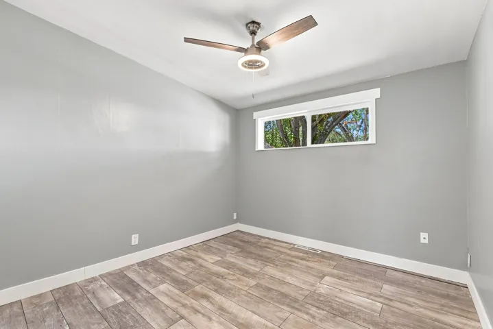 Wood-finish flooring, neutral gray wall tones, ceiling fan, and a transom window
