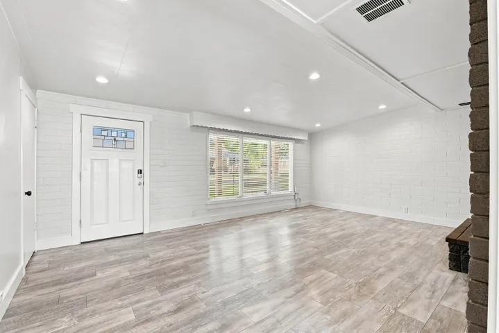 Bright living area featuring wood-finish flooring, recessed lighting, and white painted brick walls