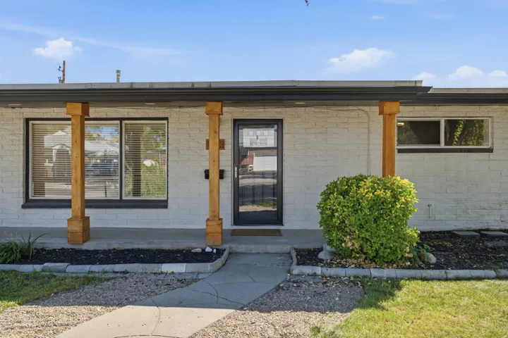 White brick exterior with natural wood-finish support columns, a dark-frame entry door, and dark-frame windows