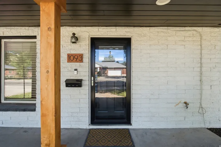 White brick exterior with a natural wood post, black front door with glass insert, and an outdoor wall sconce