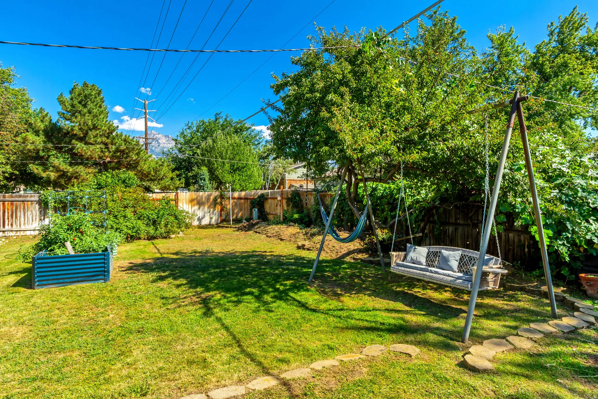 Expansive fenced backyard featuring a manicured lawn, established landscaping, and a raised garden bed