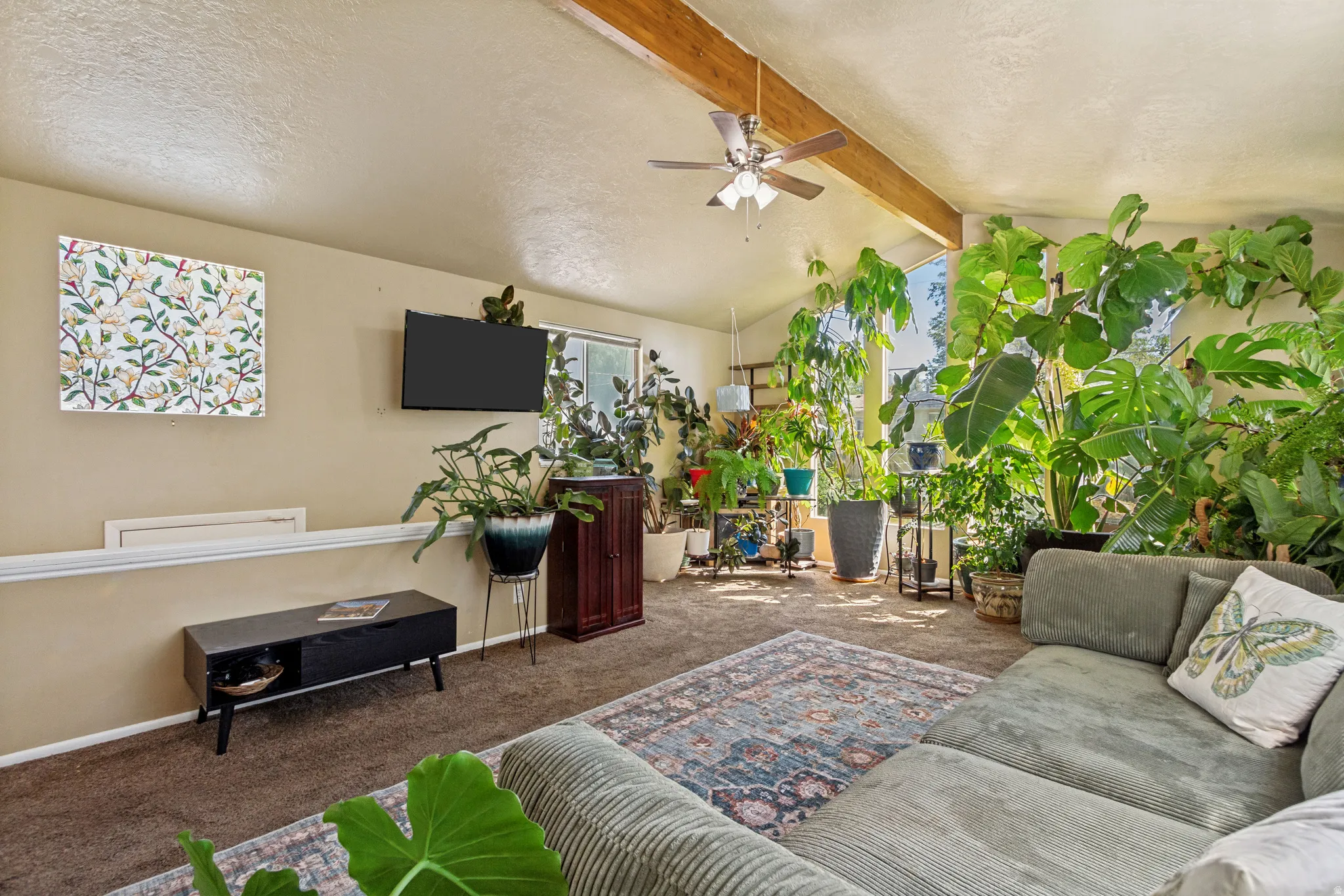 Vaulted ceiling with exposed wood beams, ceiling fan, and carpeted flooring
