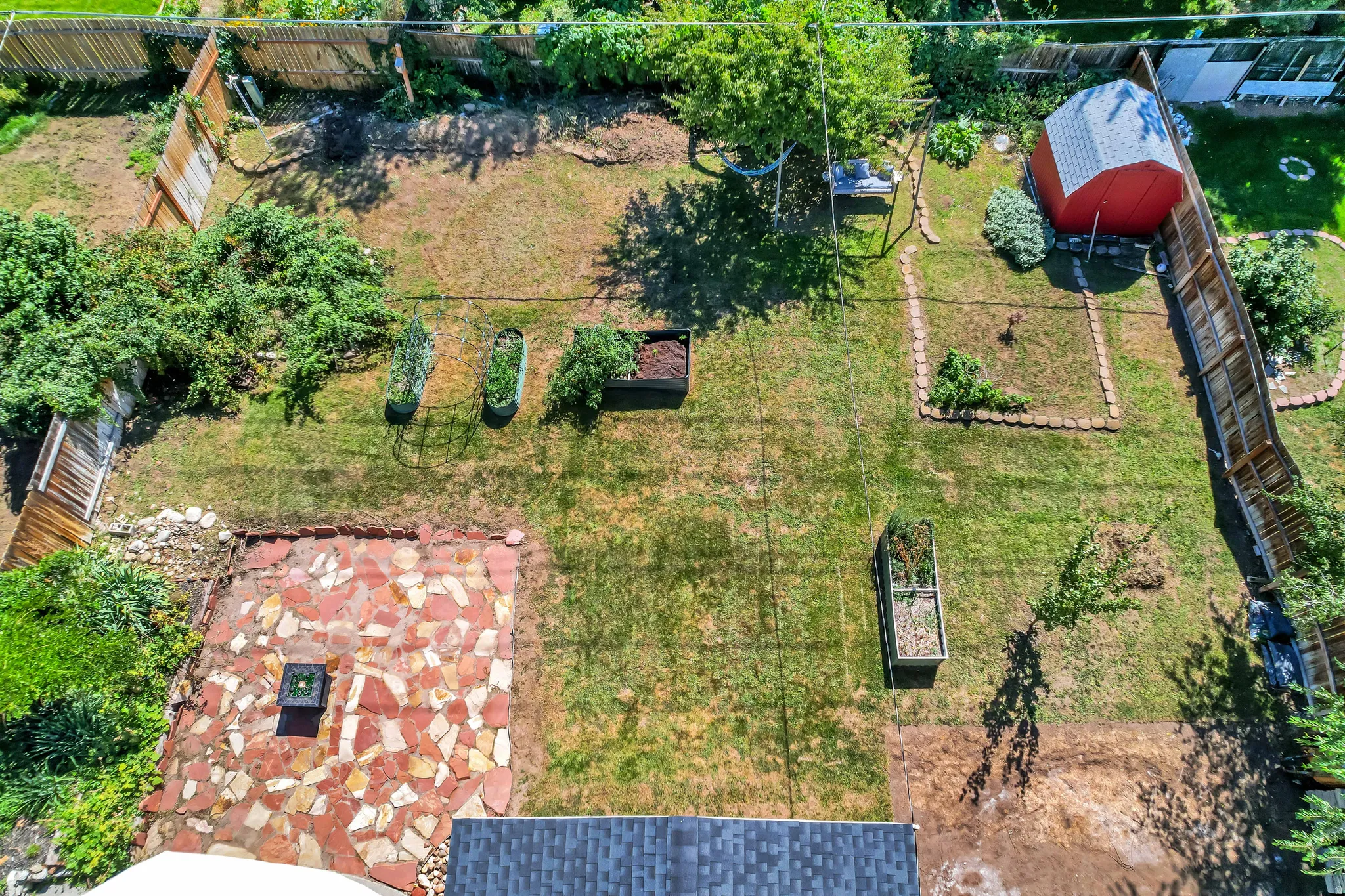 Expansive backyard featuring a stone patio with a fire pit, a red storage shed, raised garden beds, and a wood privacy fence