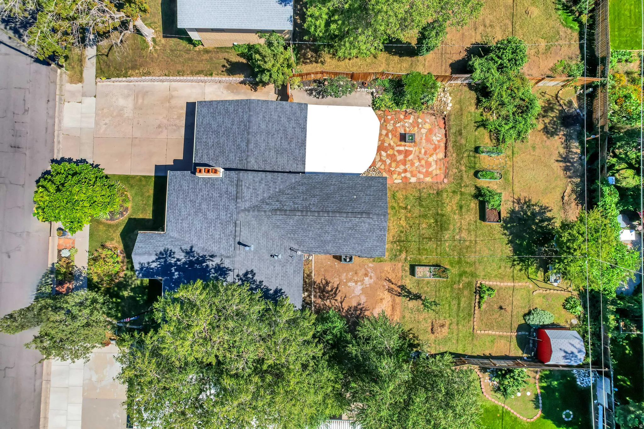 Asphalt shingle roofing, paved driveway, expansive lawn, mature trees, and a flagstone patio area