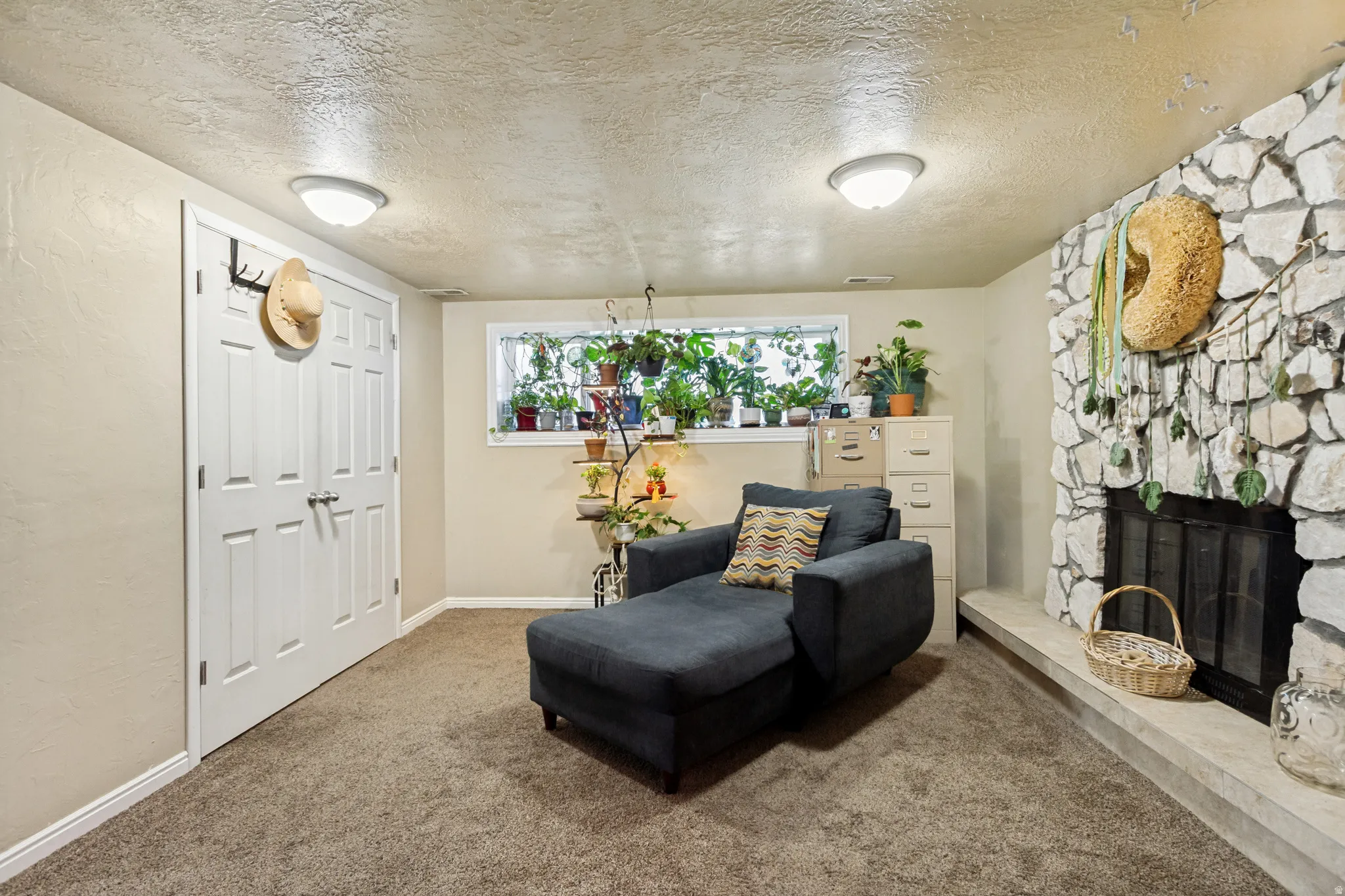 Finished basement recreation room featuring neutral carpet flooring, recessed ceiling lighting, a decorative fireplace with stone surround, and a high transom window with natural light