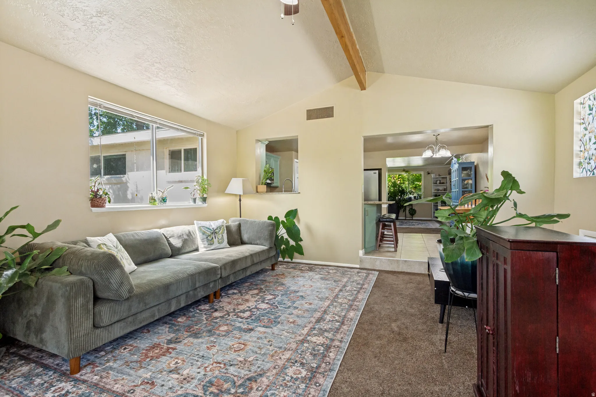 Vaulted ceiling with exposed wood beams, large windows, and a cased opening