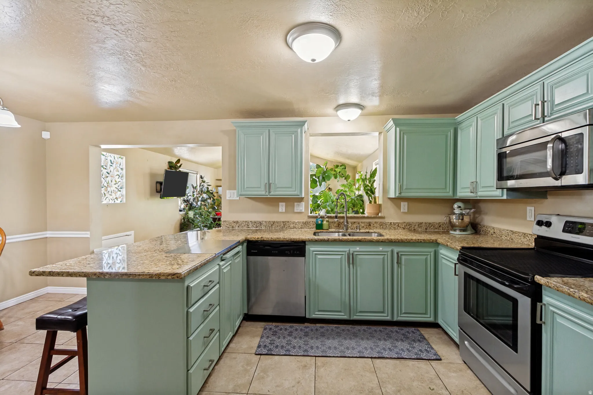 Kitchen featuring a U-shaped countertop, light green cabinetry, stainless steel appliances, and a pass-through window