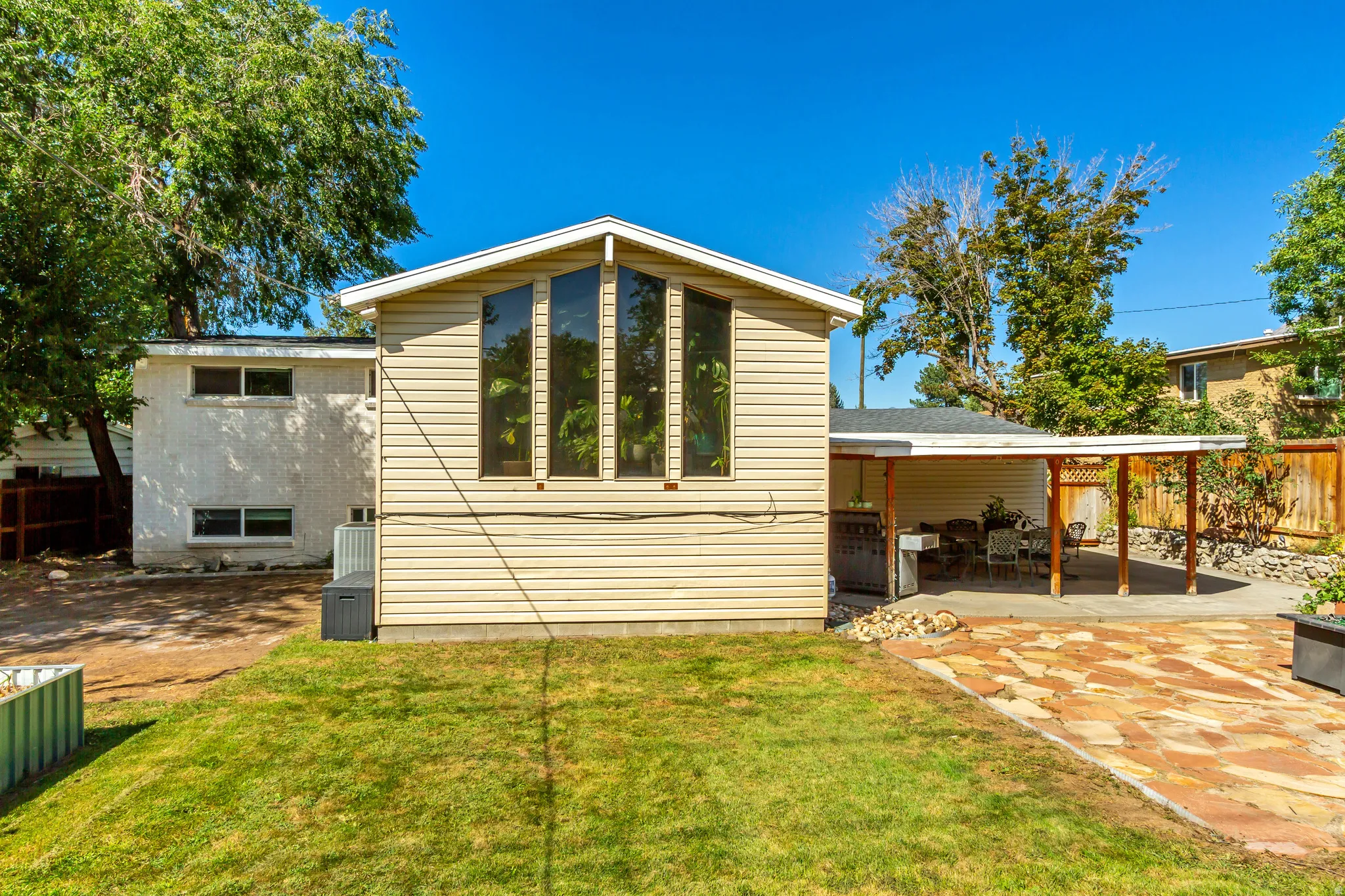 Rear exterior with vertical pane windows, a covered patio structure, and a flagstone patio area