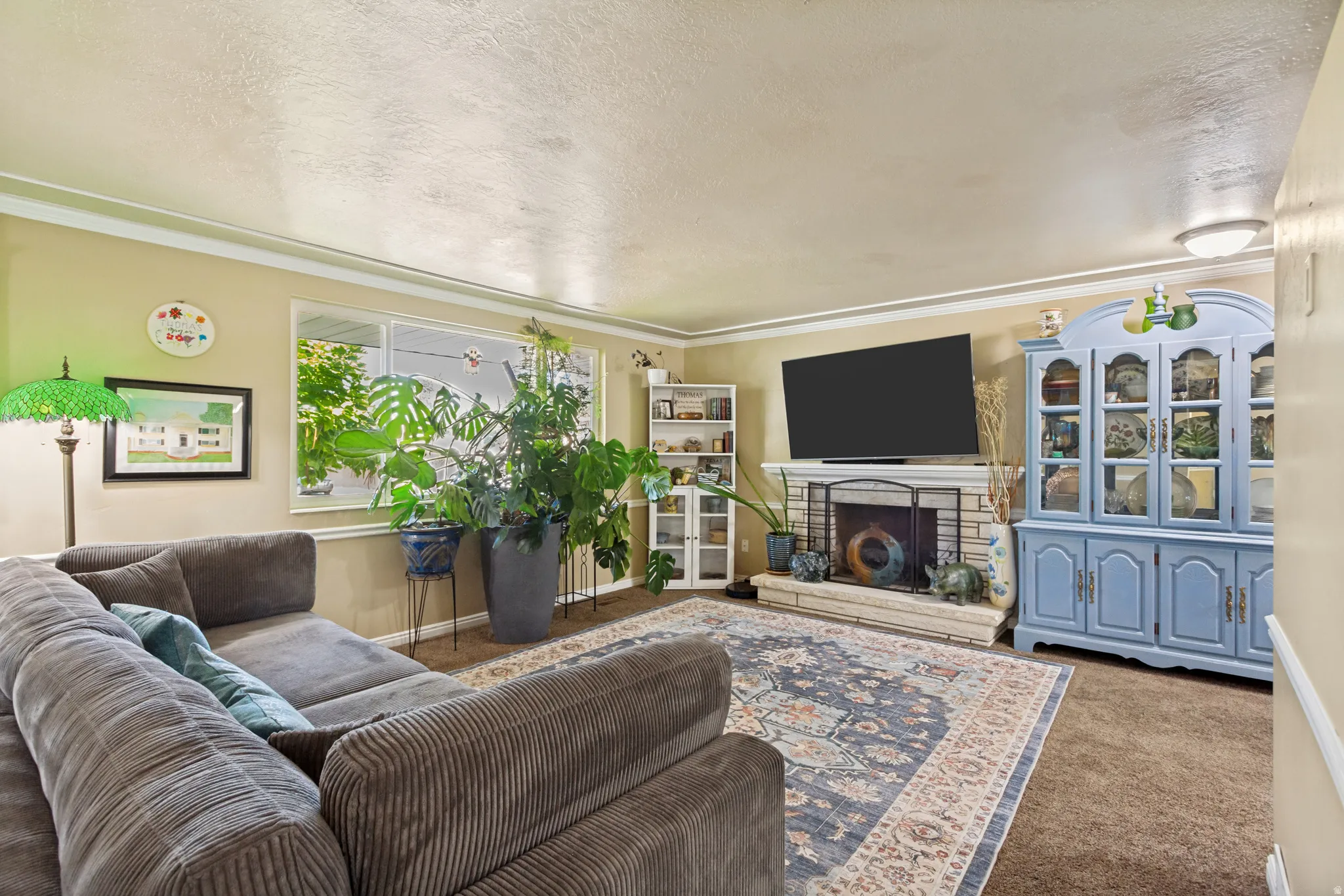 Living area with a window, crown molding, and a fireplace featuring a stone surround and hearth