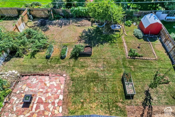 Expansive lawn featuring a flagstone patio, raised garden beds, mature trees, and a red storage shed