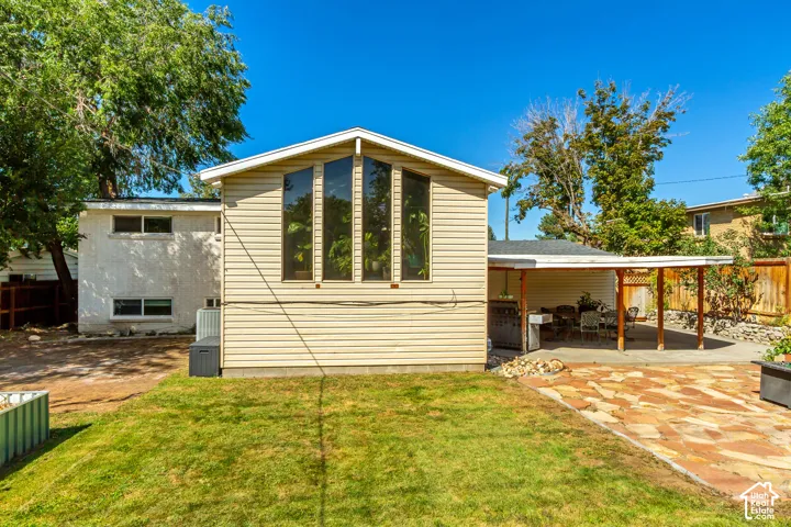 Rear exterior with vertical pane windows, a covered patio structure, and a flagstone patio area
