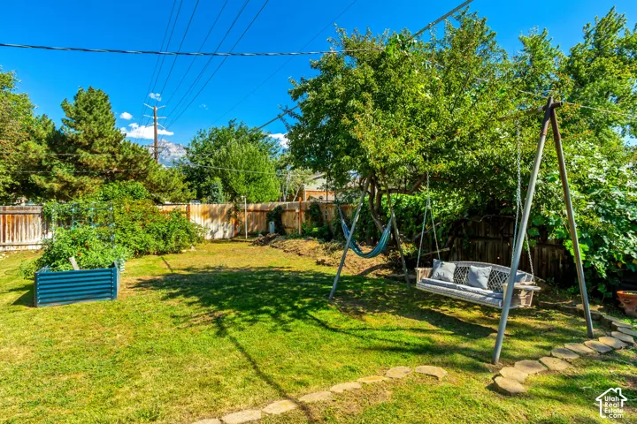 Expansive fenced backyard featuring a manicured lawn, established landscaping, and a raised garden bed